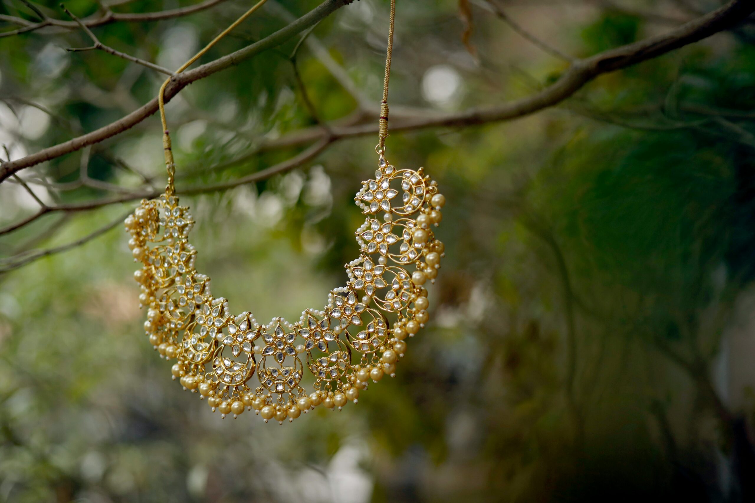 Luxurious gold bridal necklace with pearls and intricate design hanging elegantly on a tree branch.